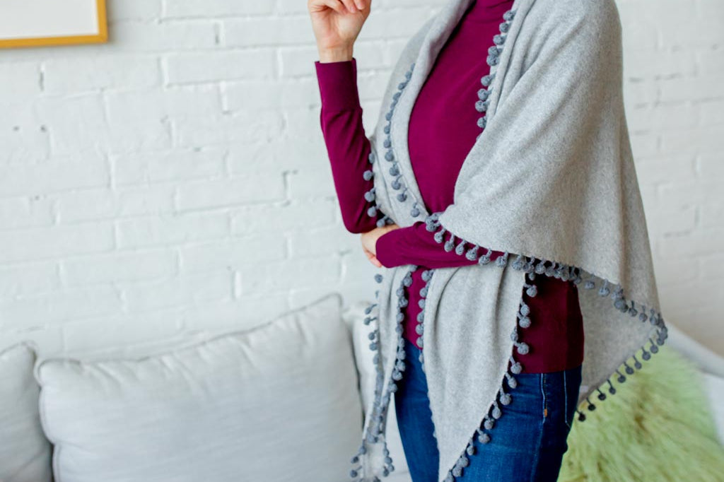 Model Wearing Alpine Cashmere Pom-Pom Triangle Wrap in Birch and Flannel Gray