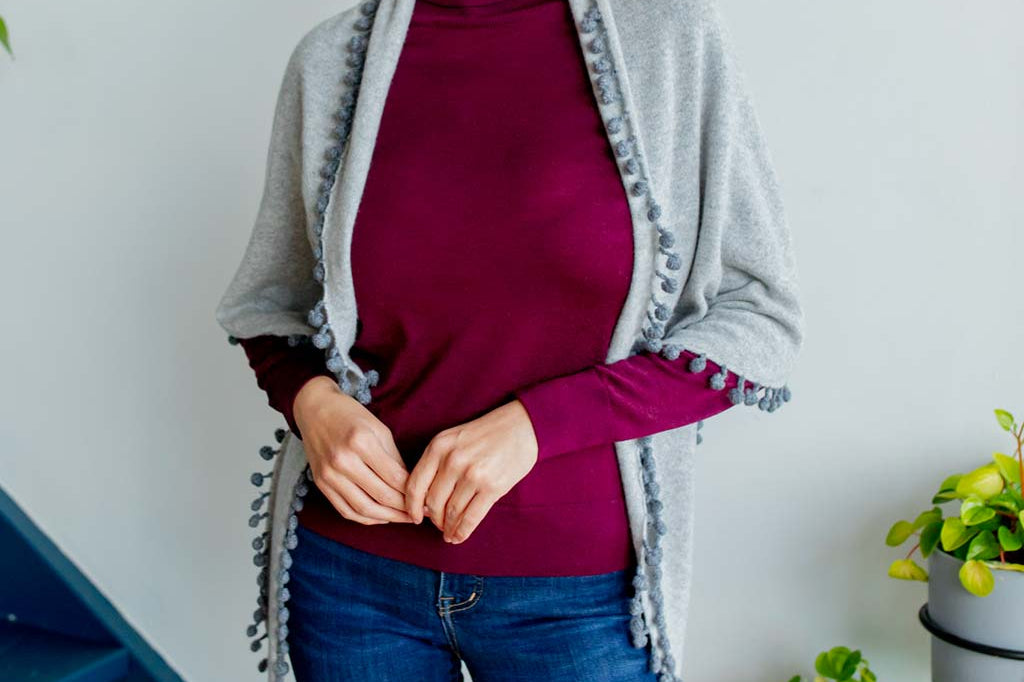 Model Wearing Alpine Cashmere Pom-Pom Triangle Wrap in Birch and Flannel Gray