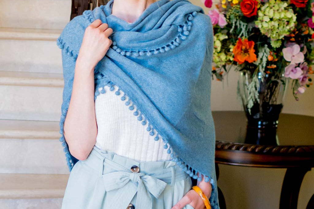 Model Wearing Alpine Cashmere Pom-Pom Triangle Wrap in Stonewash Blue